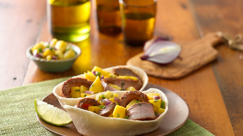 Old El Paso Soft Tortillas Bowls filled with steak and mango salsa with a wooden background.