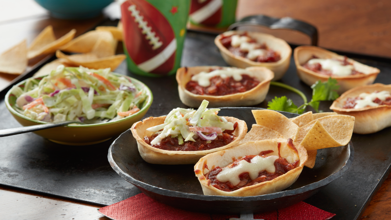 Old El Paso Mini Soft Tortilla Bowls filled with barbecue pork and cheese melted in a football stripe shape on a black wooden serving board.