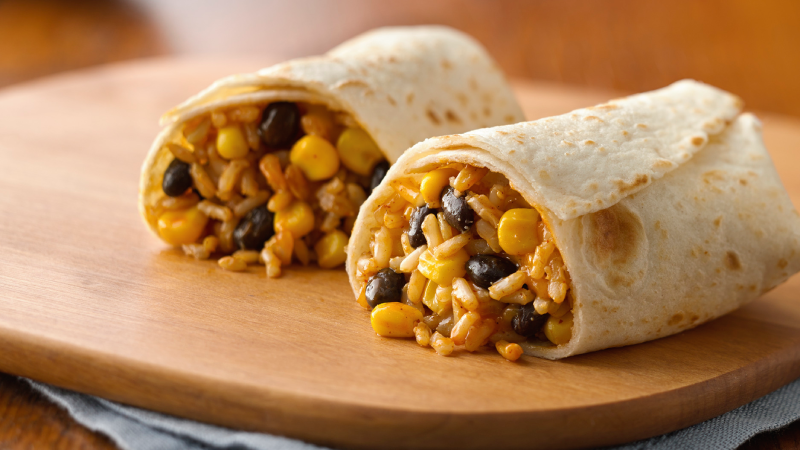 Two burritos on a wooden board filled with rice, corn and black beans